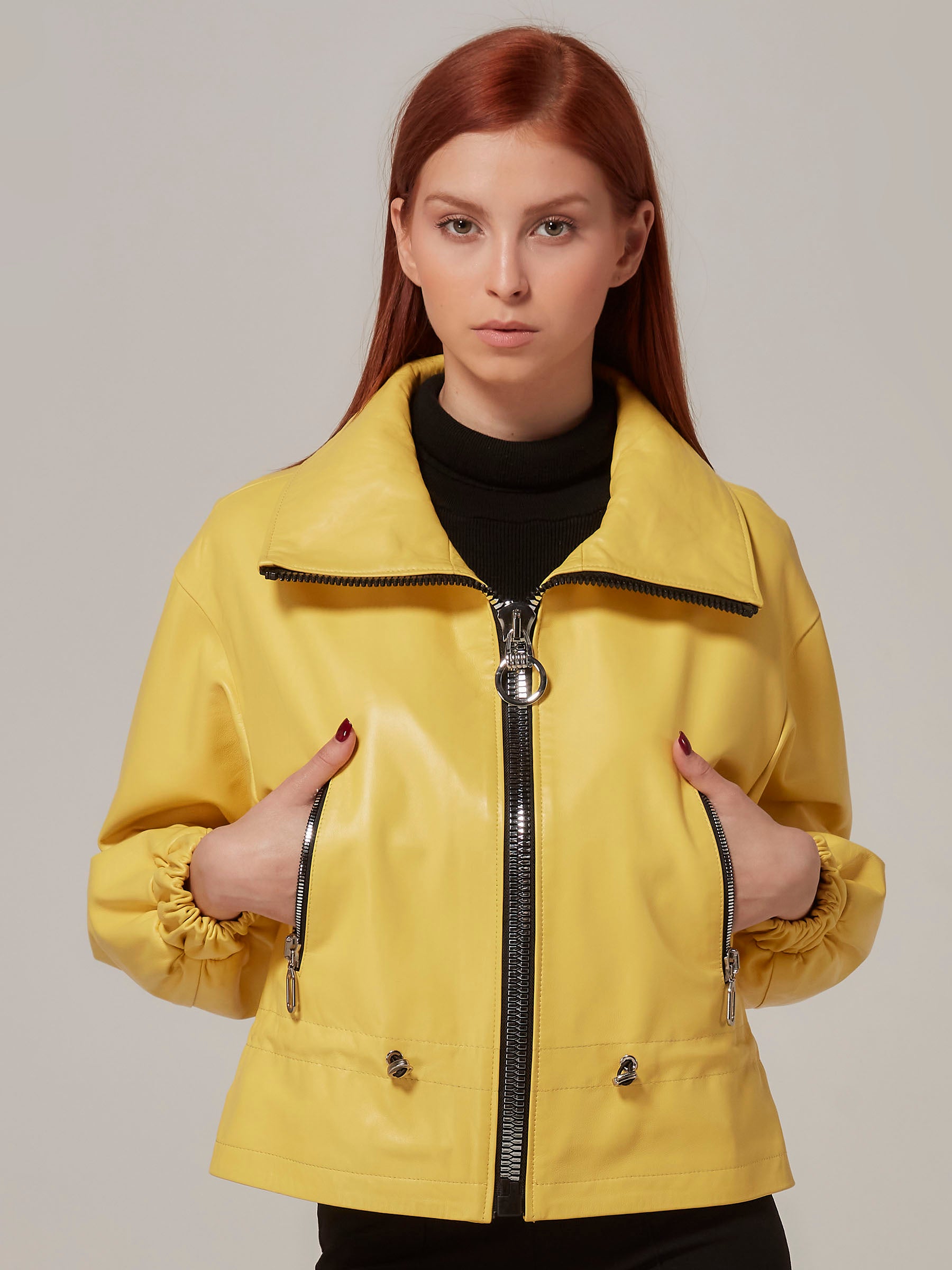 A woman wearing a yellow leather jacket with elastic cuffs and a belt, paired with black pants.